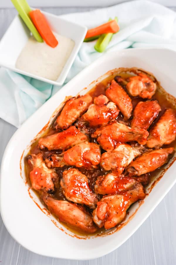 Baked BBQ Chicken Wings in a white dish next to carrot and celery sticks in sauce