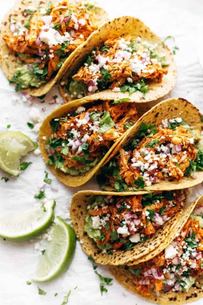 chicken tinga tacos next to lime wedges on a white background