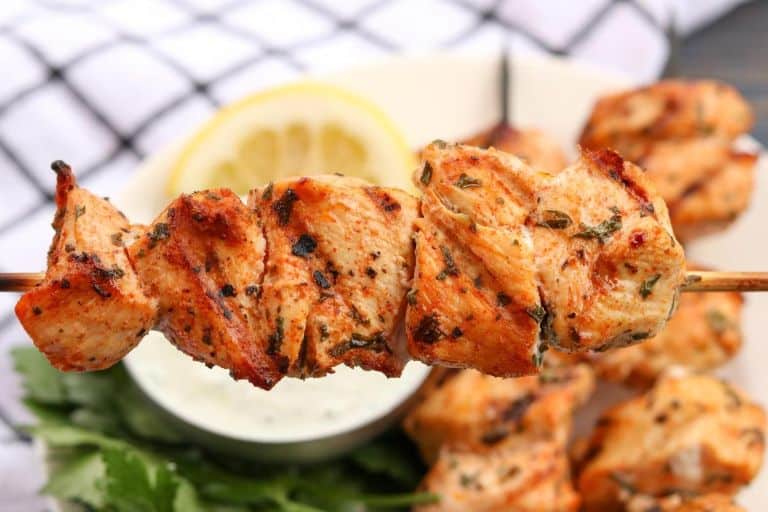grilled lemon herb chicken skewer with more skewers and homemade tzatziki sauce in the background