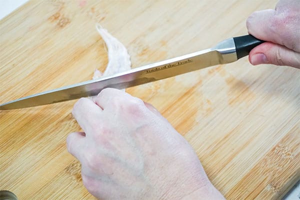 a person using a knife to cut a chicken wing on a wood cutting board