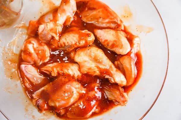 chicken wings and bbq sauce in a glass bowl on a white background