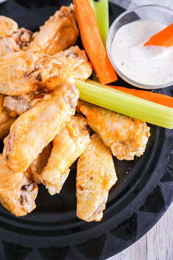 buffalo chicken wings next to carrot and celery sticks and a bowl of sauce on a black plate