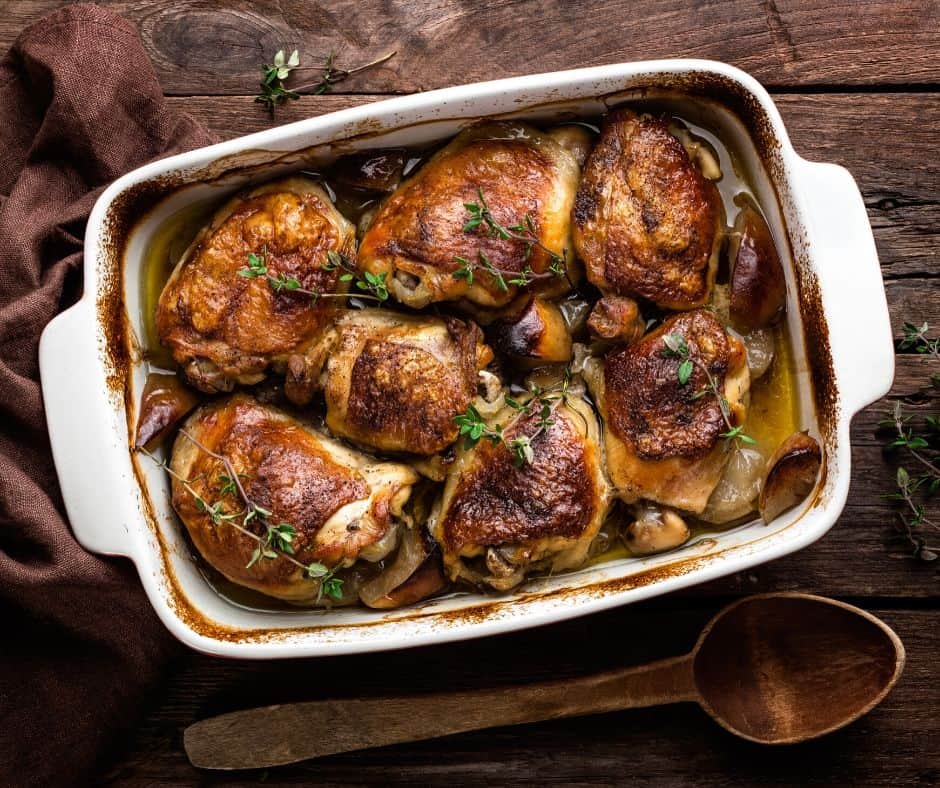 chicken thighs in a white baking dish next to a wooden spoon on a wood table