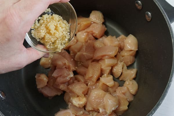 seasoning being poured from a glass bowl into a pot of raw cubed chicken