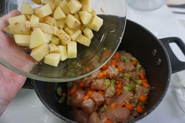 diced potatoes being added to a pot of chicken vegetable soup