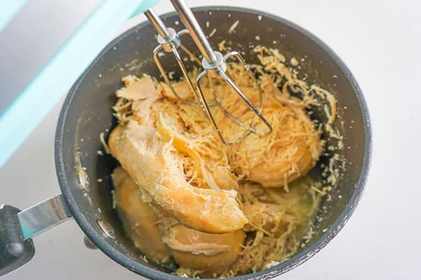 beaters being used to shred chicken breasts in a skillet