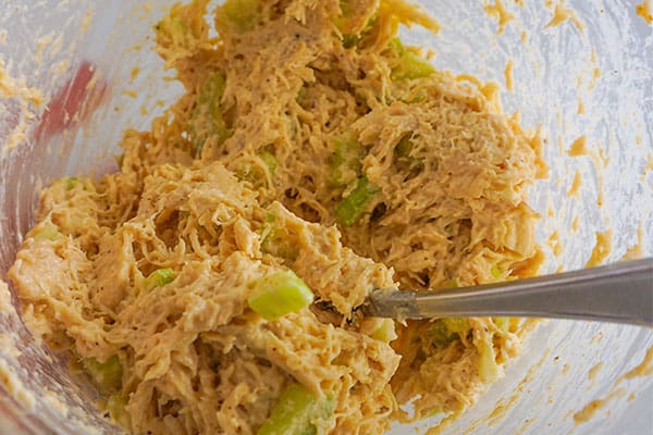 cheese being folded into the chicken salad mixture in a glass bowl