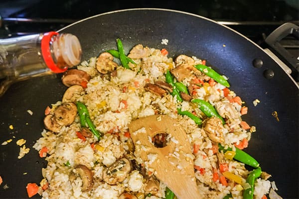 soy sauce being added to chicken fried rice cooking in a skillet