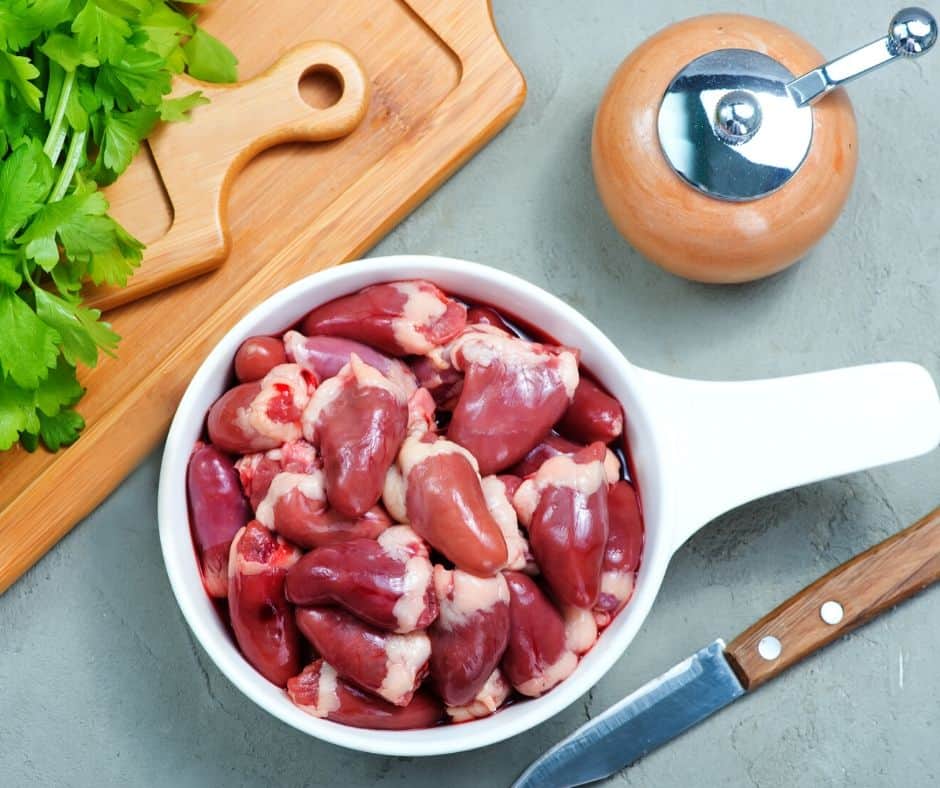 raw chicken giblets in a white bowl next to a knife and cutting boards