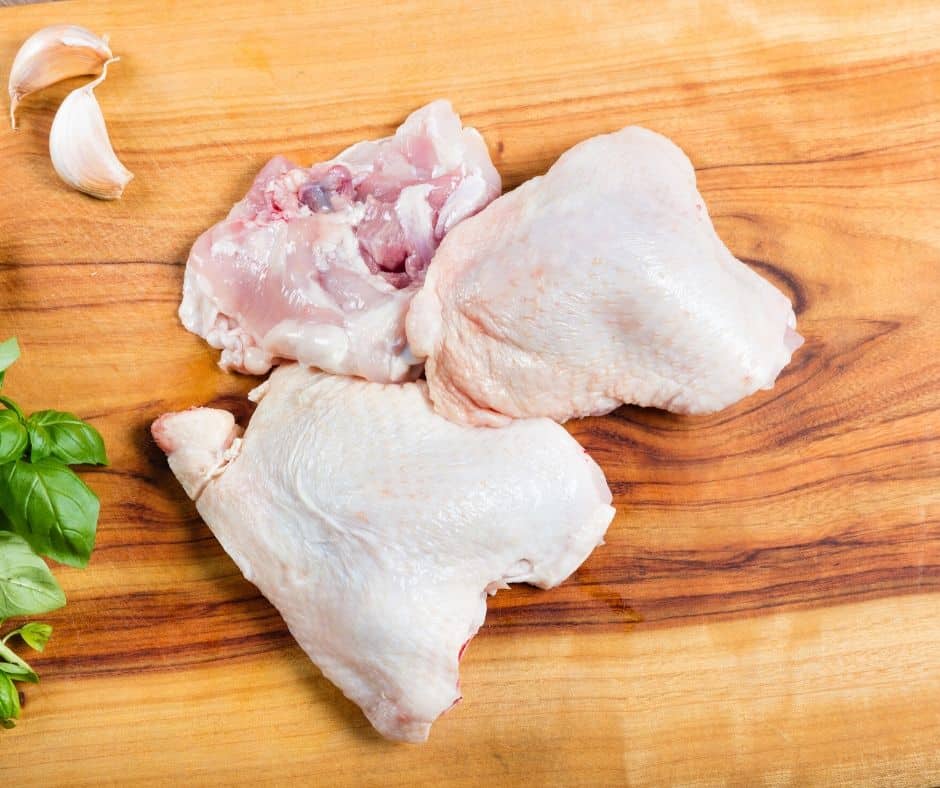 raw chicken thighs next to garlic cloves on a wooden board