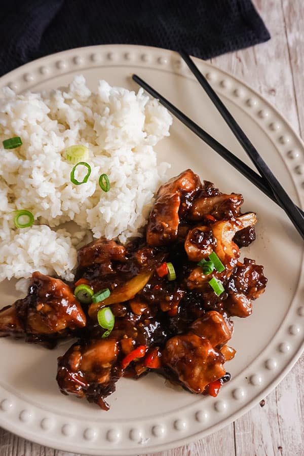 Spicy General Tso’s Chicken next to white rice and black chopsticks on a white plate