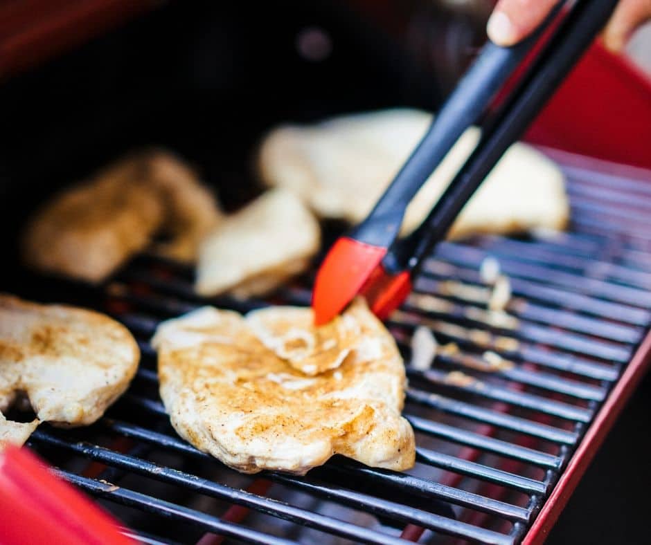 a person using a tong to turn over a piece of chicken on a grill