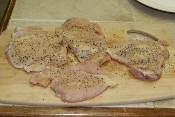 raw chicken breasts rubbed with seasonings on a wooden cutting board