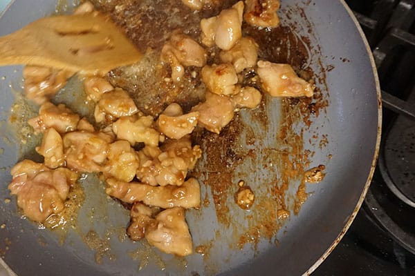 a wooden spatula being used to stir orange chicken being cooked in a pan