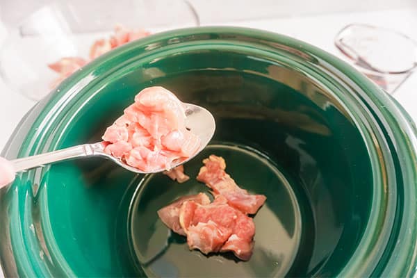 raw chicken being added to sesame oil in a slow cooker