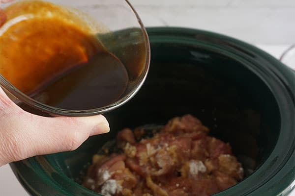 sauce being added to raw chicken in a slow cooker