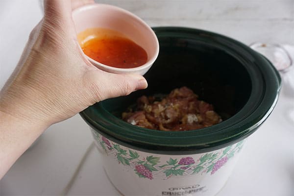 chili sauce being added to raw chicken in a slow cooker