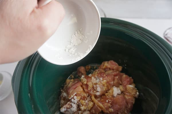 cornstarch being added to raw chicken in a slow cooker