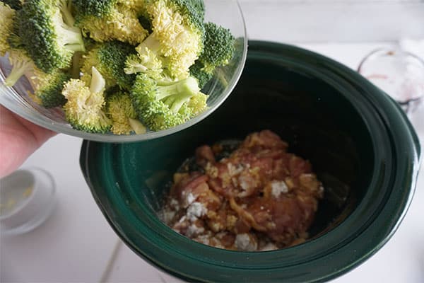 broccoli florets being added to a chicken mixture in a slow cooker