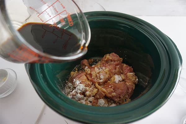soy sauce being added to a chicken mixture in a slow cooker