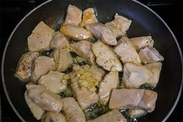 chicken, garlic and seasoning cooking in a skillet