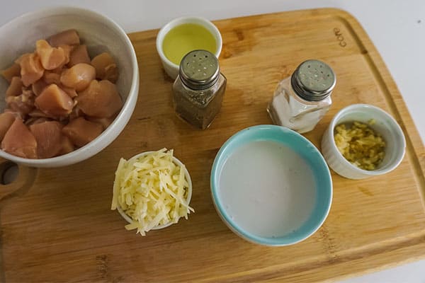 ingredients in a bowl on a wooden cutting board needed to make Homemade Chicken Alfredo next to olives and a fork on a red plate