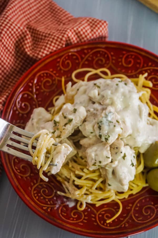 Homemade Chicken Alfredo next to olives and a fork on a red plate