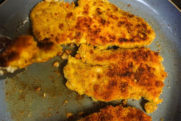 breaded chicken breasts being cooked in a skillet