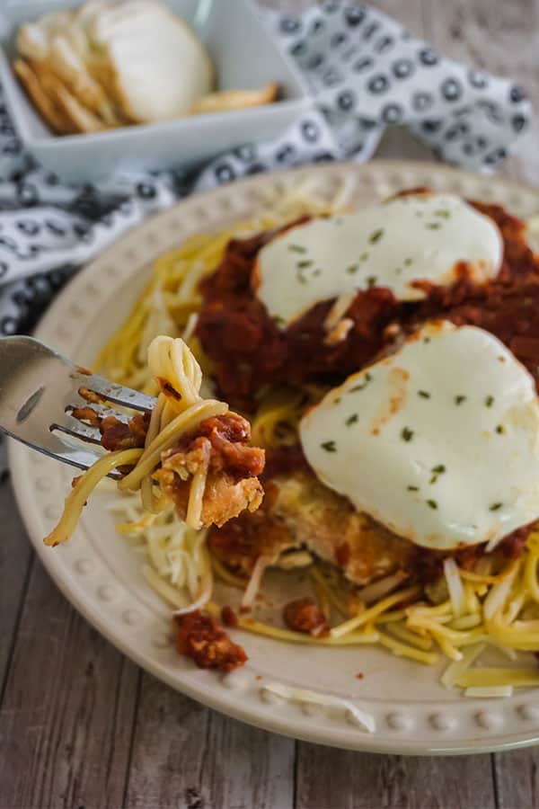 a forkful of Homemade Chicken Parmesan above a plate full of the Homemade Chicken Parmesan on a wood table 