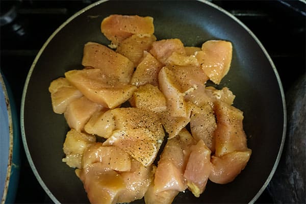 diced raw chicken breasts and seasonings cooking in a skillet