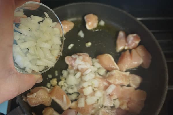 diced onions being added to diced raw chicken breasts and seasonings cooking in a skillet