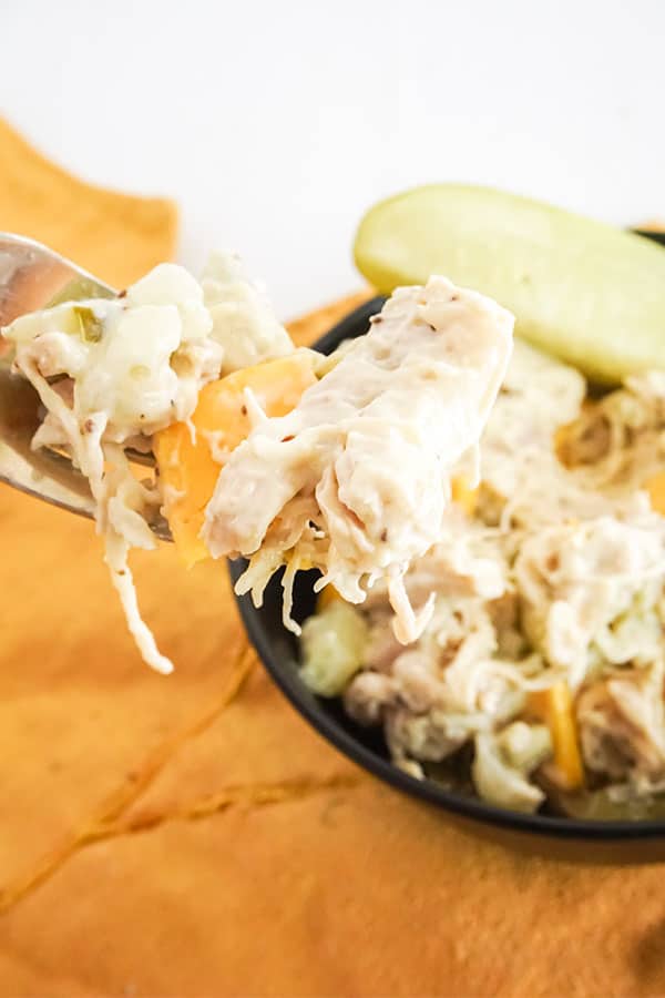 a fork holding some Homestyle Chicken Salad above more chicken salad next to a pickle in a black bowl 