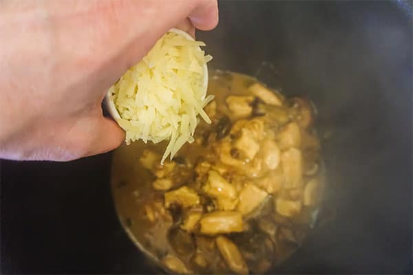 a hand adding shredded mozzarella to the roux in a slow cooker