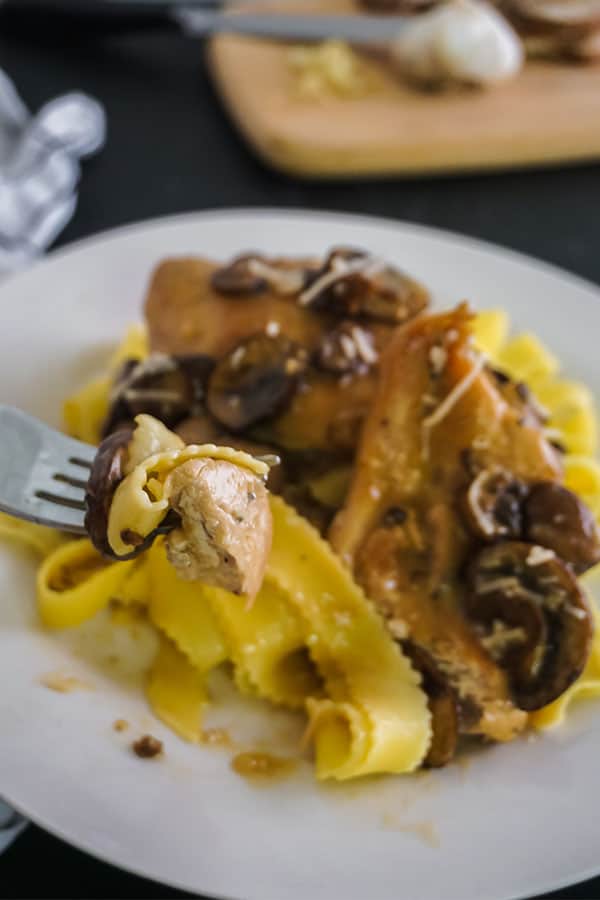 a forkful of Slow Cooker Chicken Marsala above more of the meal on a white plate
