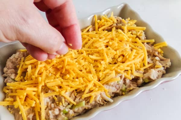 chicken enchilada dip mixture being topped with shredded cheese