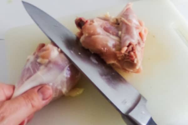 a person using a knife to debone a chicken leg and thigh on a white cutting board
