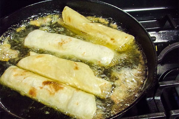 chicken taquitos cooking in a frying pan