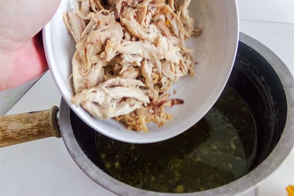 chicken being added to broth in a pot