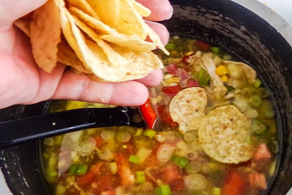 a hand adding tortilla chips to a pot of chicken tortilla soup