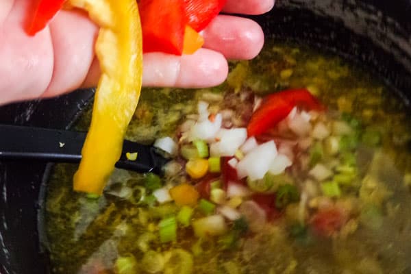 a hand adding bell pepper to chicken tortilla soup in a pot