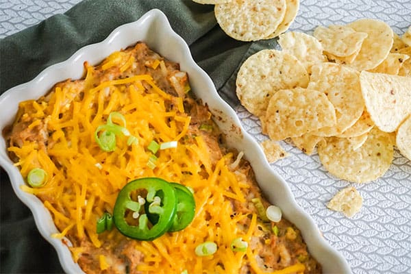 Sour Cream Chicken Enchilada Dip in a white baking dish next to some round tortilla chips on a gray cloth