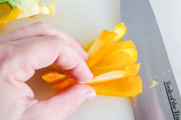 a hand holding slices of yellow bell pepper