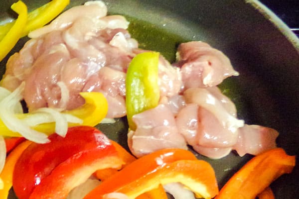  chicken, sliced bell pepper and sliced onion cooking in a pan