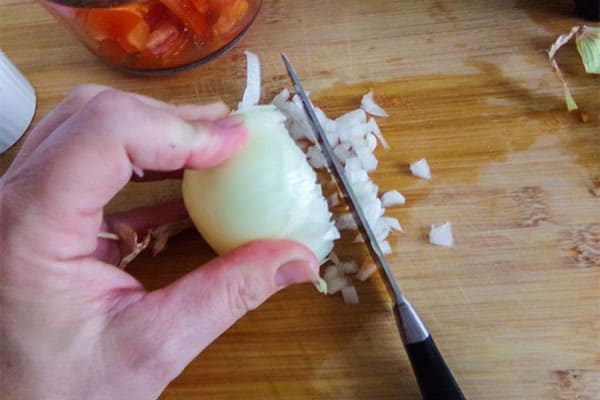 a hand dicing an onion with a knife on a wooden cutting board