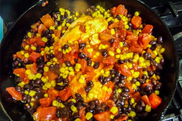 black beans on top of corn and peppers , tomatoes and chicken in a skillet