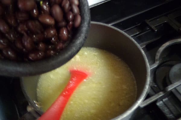 black beans being added to a pot of chicken broth