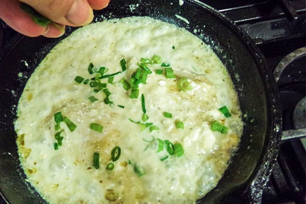a hand adding chopped green onion to Chicken Chile Verde in a skillet