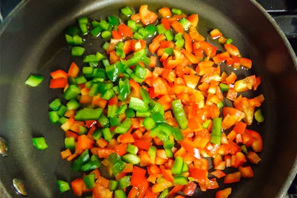 diced red and green bell pepper cooking in a skillet