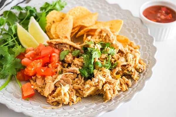 Chicken Migas on a white plate next to a fork, black and white cloth, white bowl of salsa