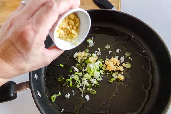 a hand adding garlic to a onions and oil in a skillet